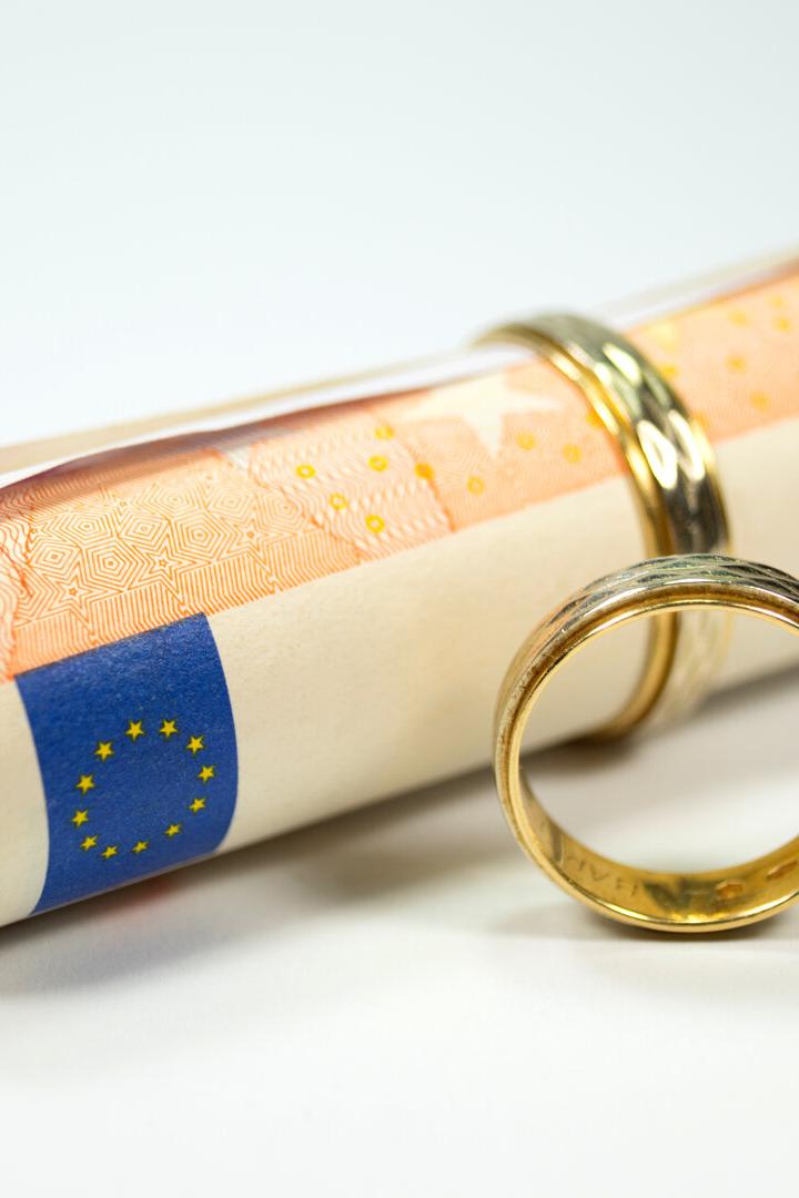 Zusammengerollte Eurobanknoten mit zwei goldenen Ringen auf weißem Hintergrund.