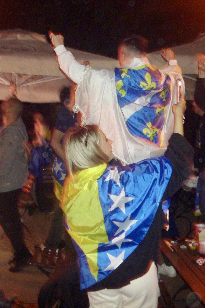 Jubelnde Menschen mit bosnischen Fahnen beim Public Viewing im Freien.