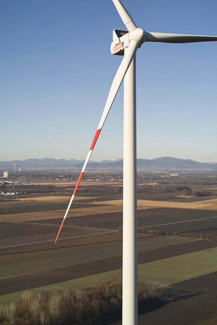 Mehrere Windkraftanlagen stehen auf weiten Feldern, eine wird gerade mit einem Kran aufgebaut, im Hintergrund Berge.