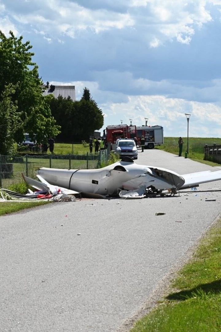 Ein abgestürztes Kleinflugzeug liegt zerstört auf einer Landstraße, Einsatzfahrzeuge und Einsatzkräfte im Hintergrund.