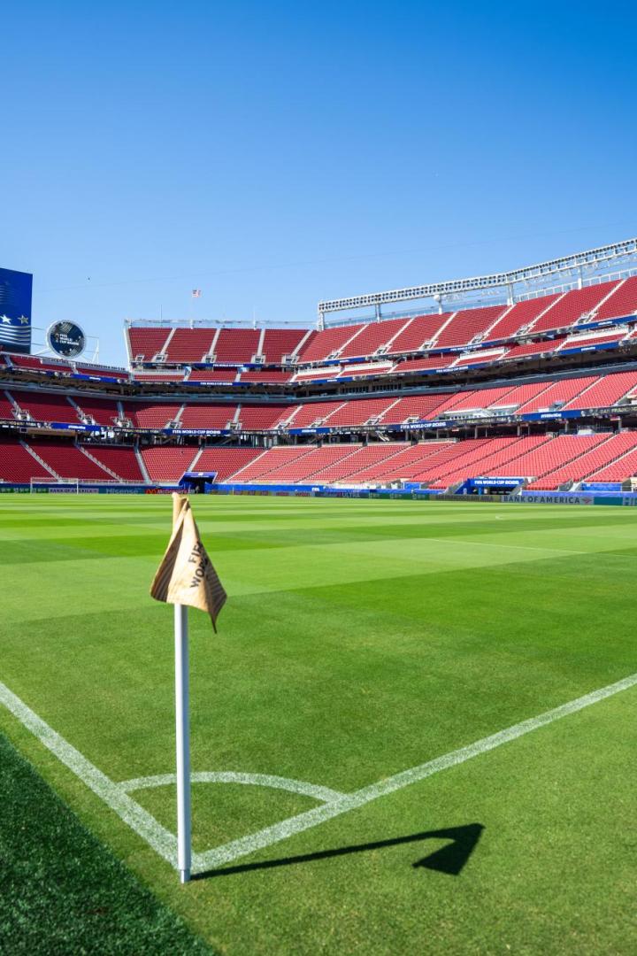 Ein leeres Fußballstadion mit roten Sitzen und einer großen Anzeigetafel für die FIFA World Cup 2026 unter blauem Himmel.