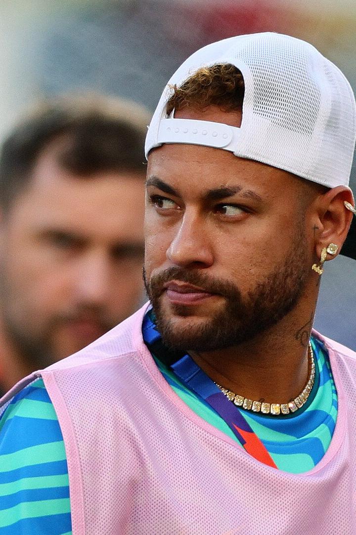 Neymar trägt eine weiße Kappe und ein pinkes Überziehshirt vor einem unscharfen Hintergrund.