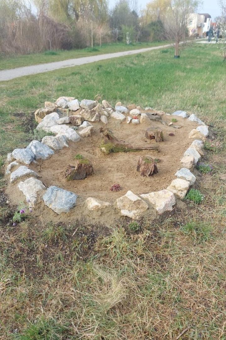Kleines rundes Steingartenbeet mit Sandfläche und Baumstümpfen im Park.