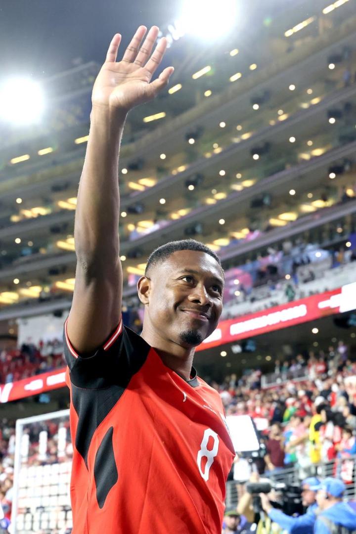 David Alaba winkt in einem roten Trikot vor jubelnden Zuschauern in einem beleuchteten Stadion.