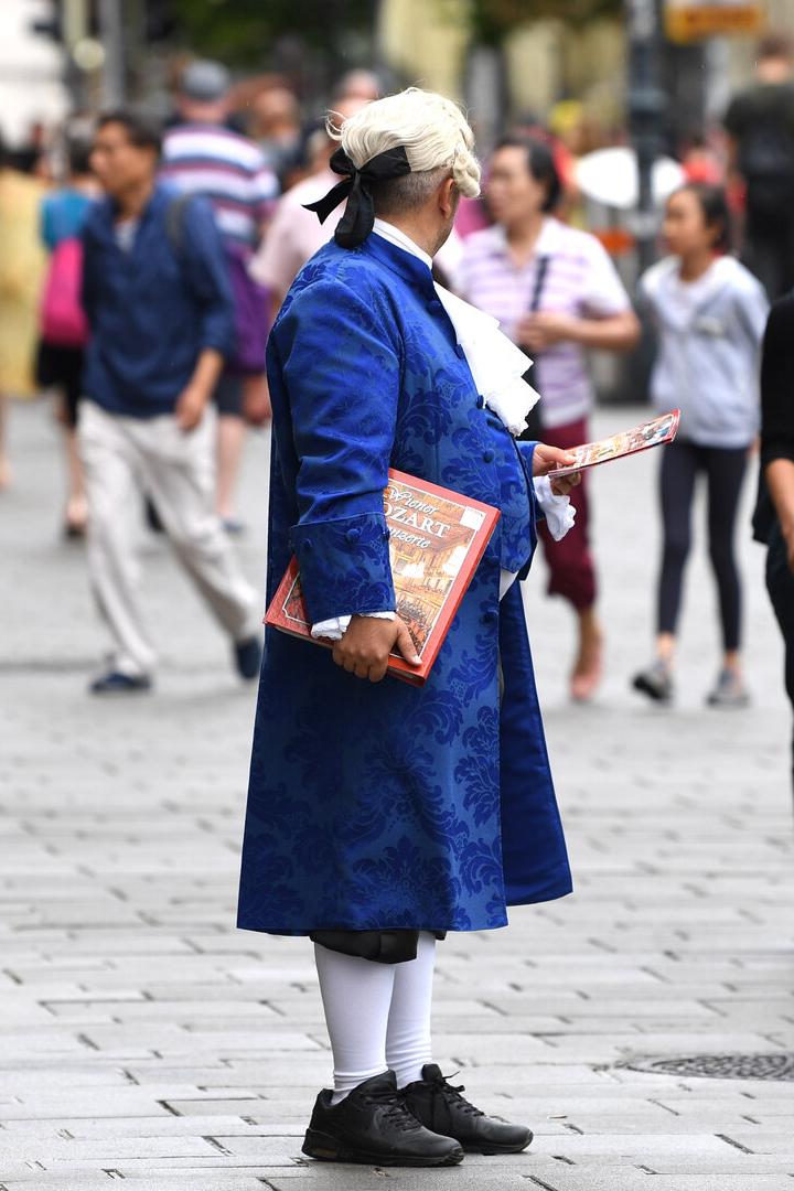 Ein Mann im blauen Barockkostüm verteilt Flugblätter auf einer belebten nassen Straße.