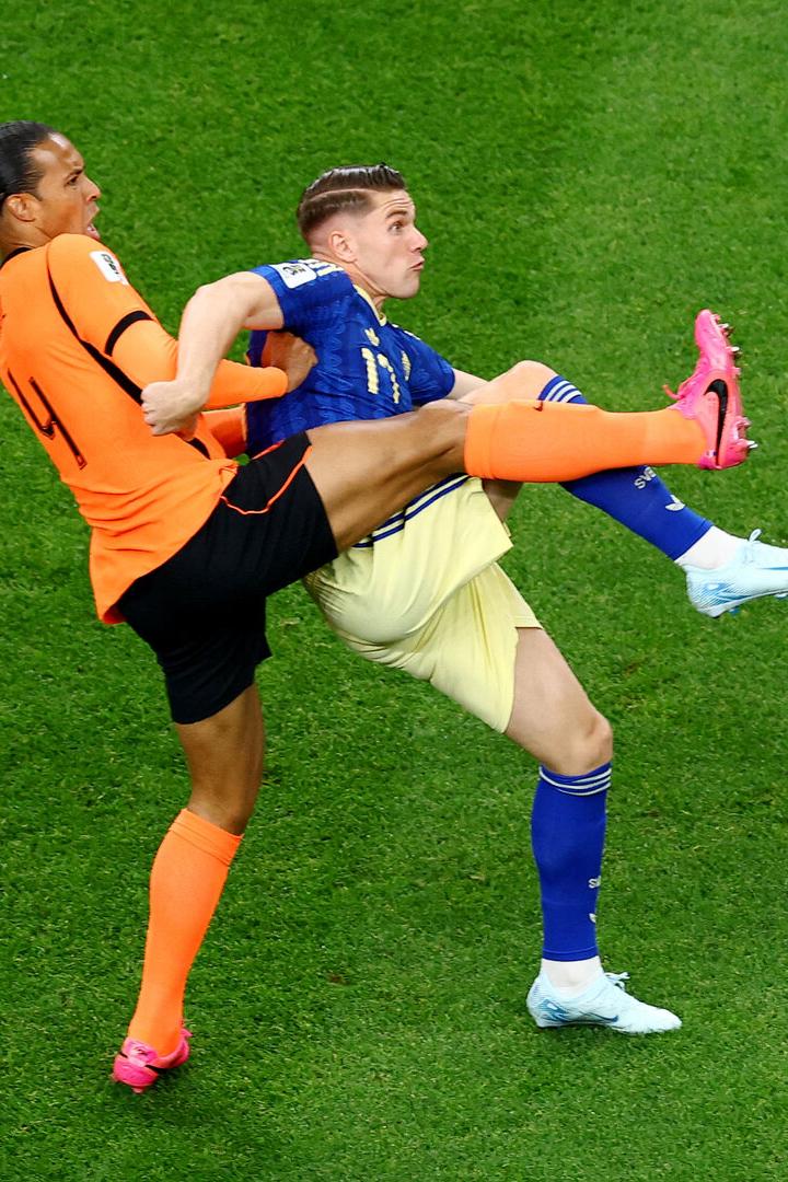 Virgil van Dijk im orangefarbenen Trikot kämpft auf dem Rasen um den Ball gegen einen Gegenspieler in Blau.