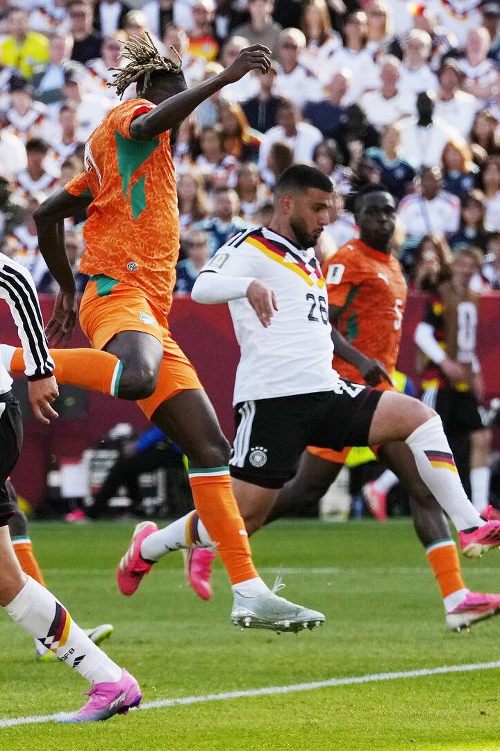 Fußballspiel mit Deutschland gegen die Elfenbeinküste, mehrere Spieler kämpfen um den Ball vor voller Tribüne.