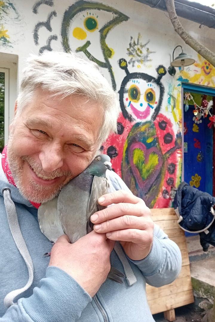 Lächelnder Mann hält eine Taube vor einer bunt bemalten Wand.