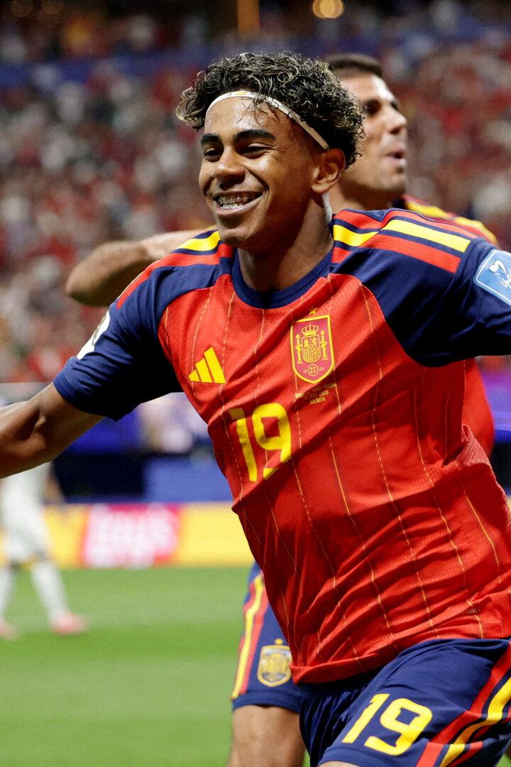 Lamine Yamal jubelt in einem roten Trikot der spanischen Nationalmannschaft auf dem Fußballfeld.