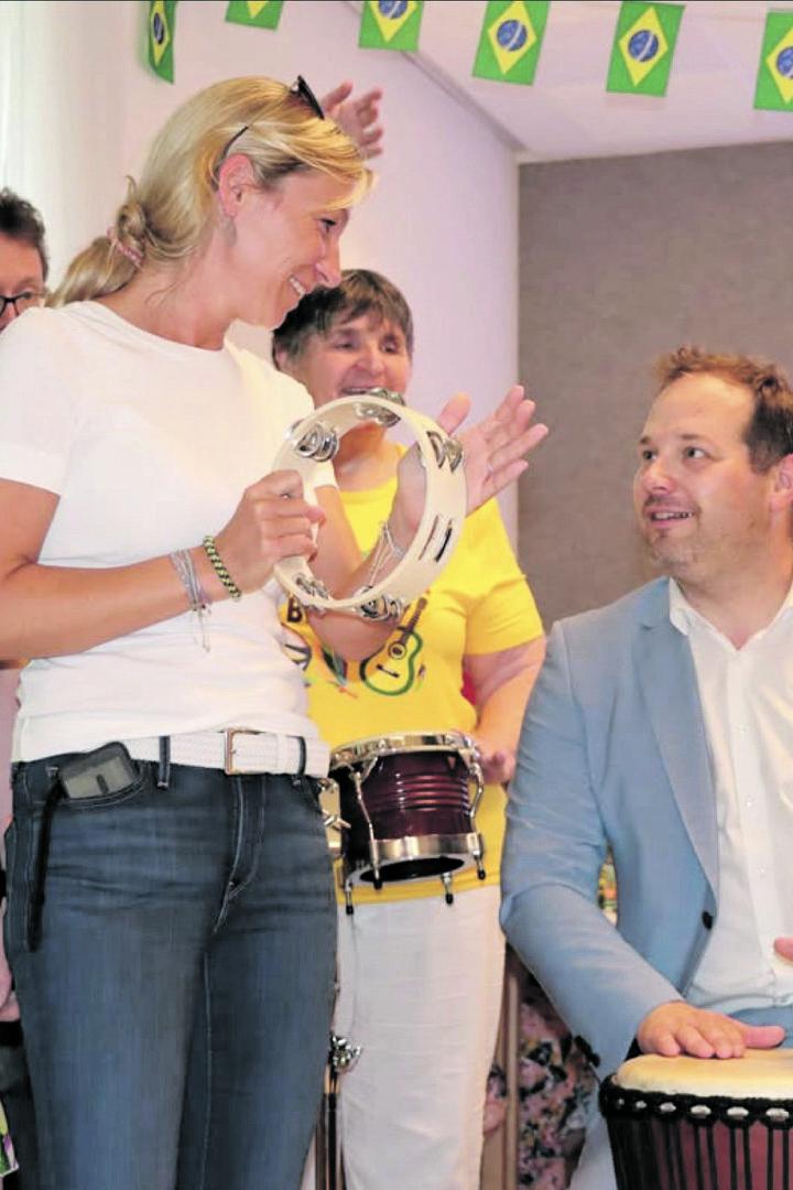 Gruppe feiernder Menschen mit brasilianischen Fahnen, mehrere halten Instrumente, ein Mann spielt Trommel.
