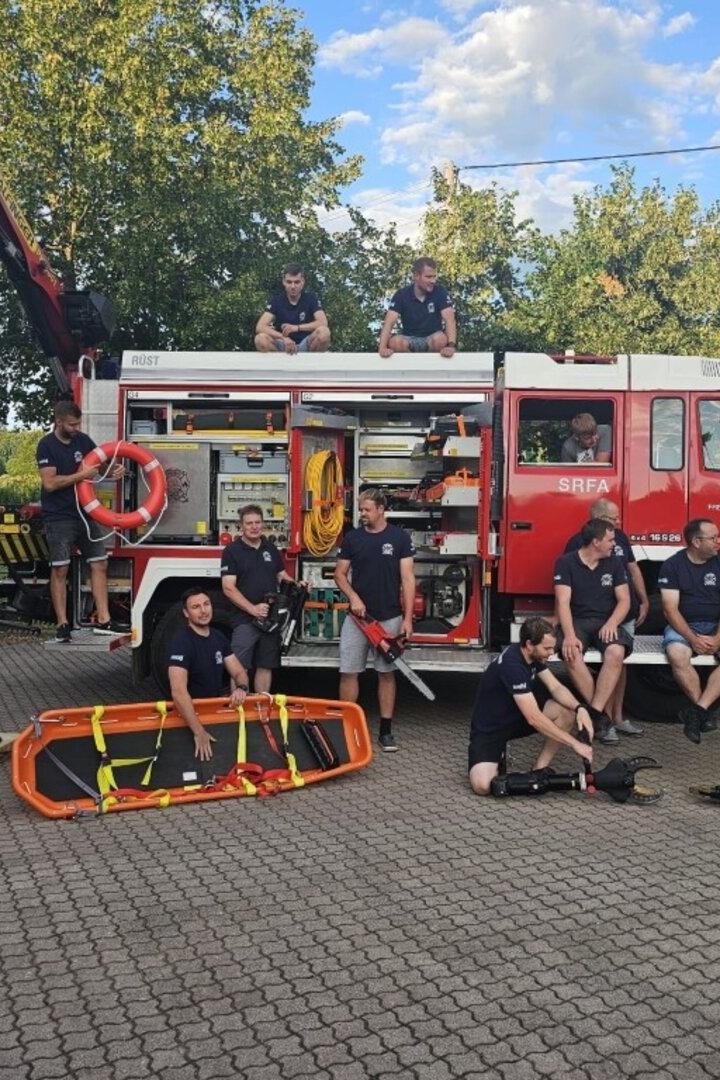 Mehrere Feuerwehrleute stehen und sitzen an einem roten Einsatzfahrzeug mit Rettungsgerät und geöffneter Geräteraumklappe.