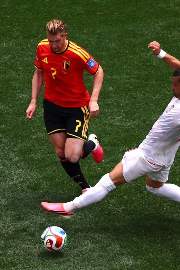 Kevin De Bruyne im belgischen Trikot kämpft auf dem Rasen um den Ball gegen einen Gegenspieler in weißer Kleidung.