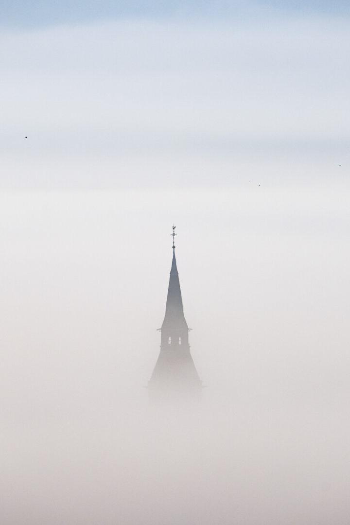 Kirchturmspitze ragt aus dichtem Nebel empor.