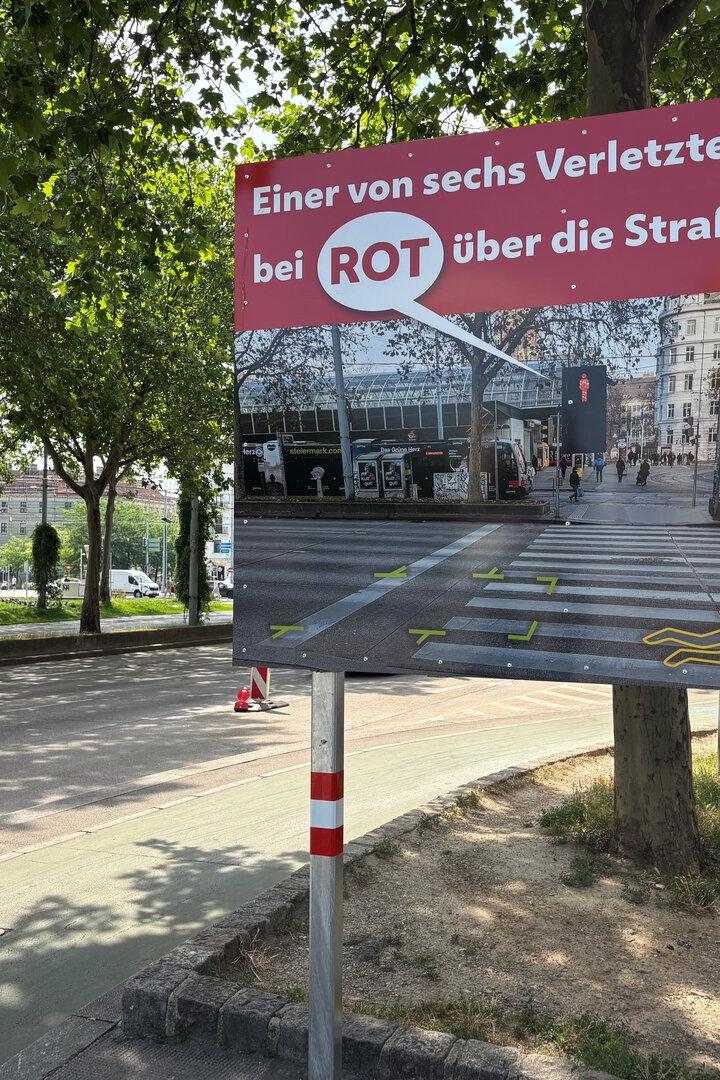 Ein Verkehrssicherheitsplakat der Stadt Wien warnt mit einer Grafik eines Zebrastreifens vor dem Überqueren der Straße bei Rot.