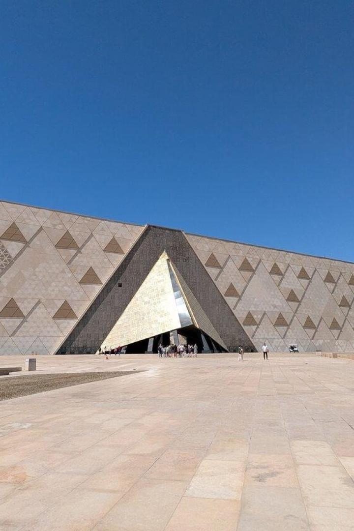 Die Fassade des Grand Egyptian Museum in Gizeh mit ihrem markanten dreieckigen Eingang vor einem klaren blauen Himmel.