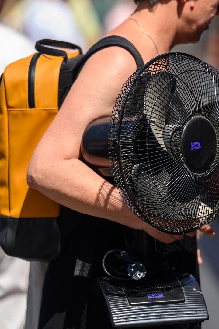 Symboldbild: Eine Person trägt einen gelben Rucksack und einen schwarzen Tischventilator der Marke SMC unter dem Arm.