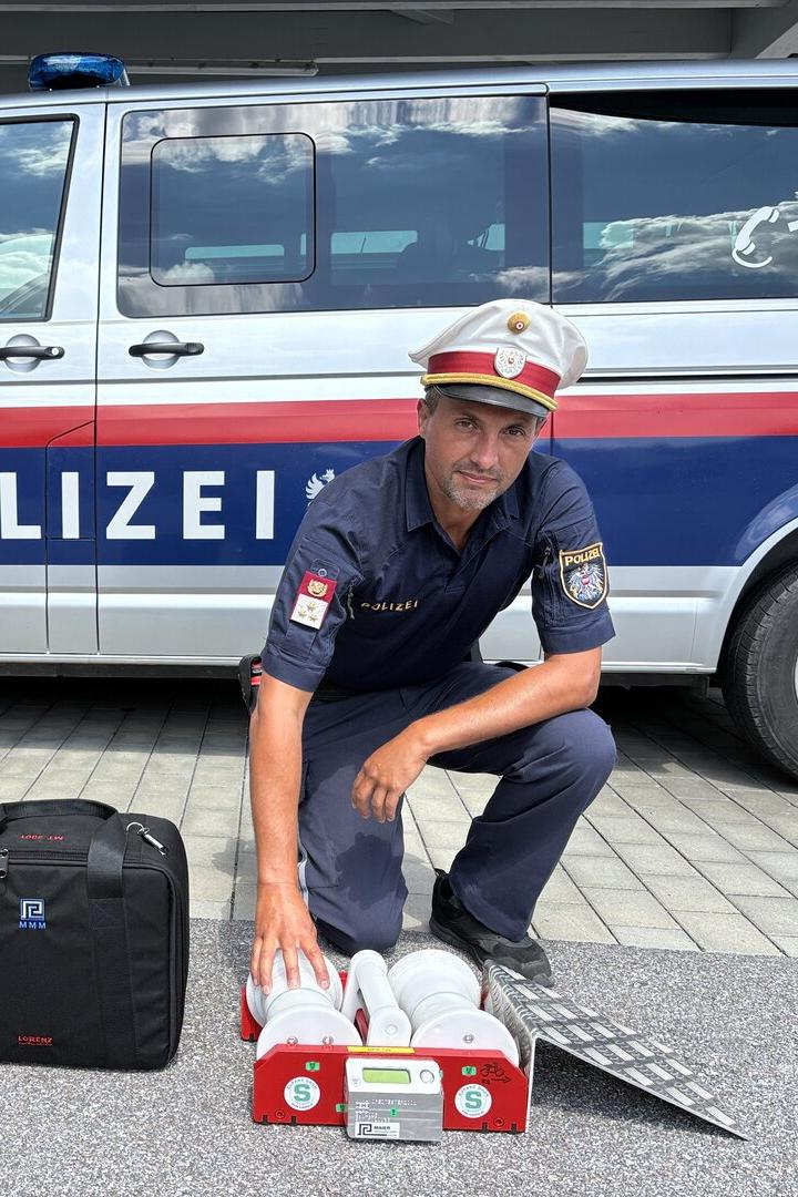 Polizist kniet vor einem Polizeiwagen neben Einsatzgerät und Tasche.