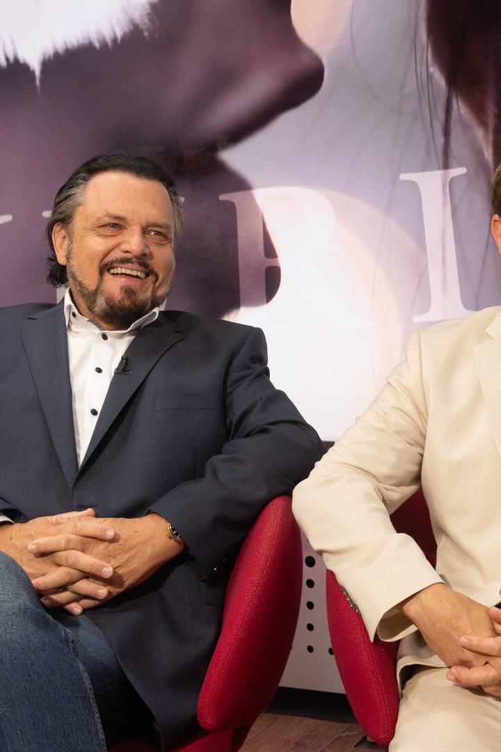 Werner Auer und Erich Furrer im Gespräch sitzen lachend in roten Sesseln, der eine in dunklem, der andere in hellem Anzug.