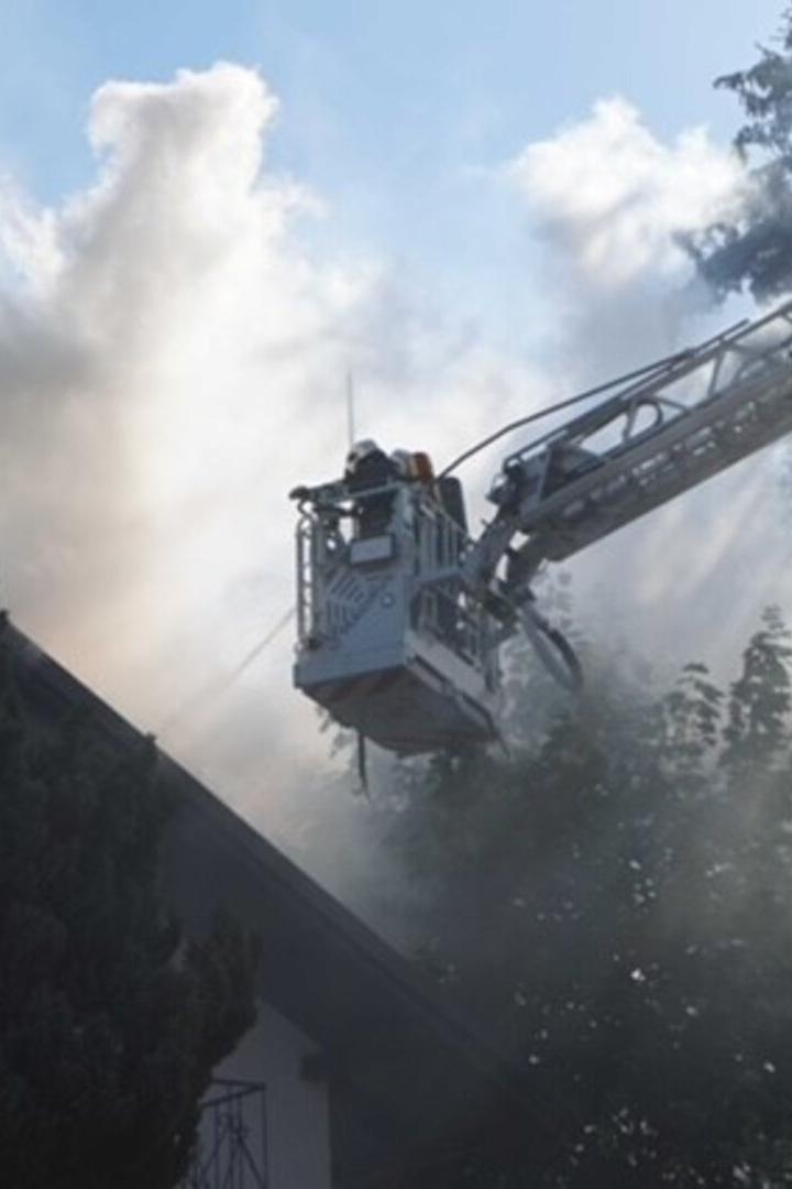 Feuerwehr löscht Brand an einem Dach mit Drehleiter, Rauch steigt auf.
