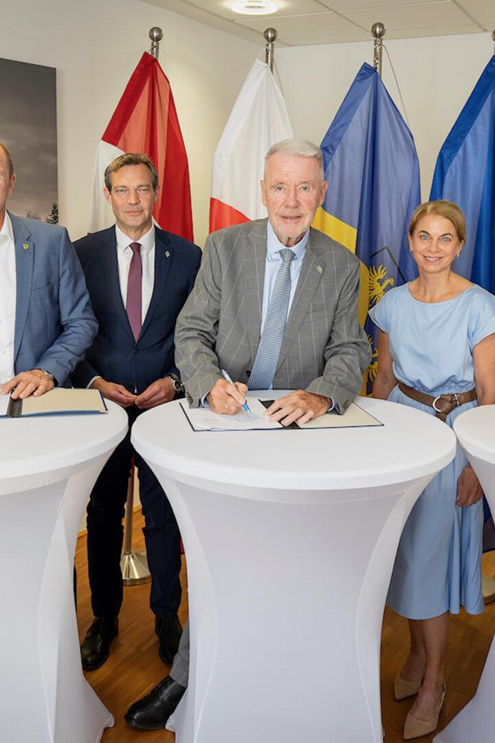 Sechs Personen stehen vor Fahnen