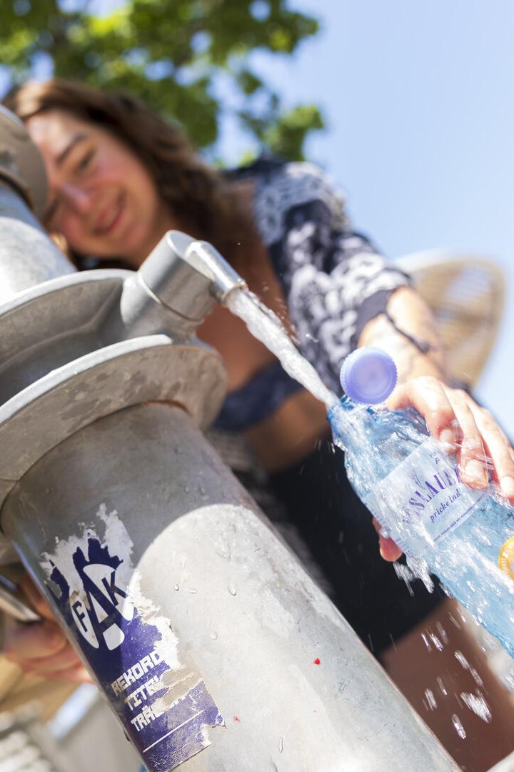Eine junge Frau füllt an einem öffentlichen Trinkwasserbrunnen eine Plastikflasche der Marke Vöslauer auf.