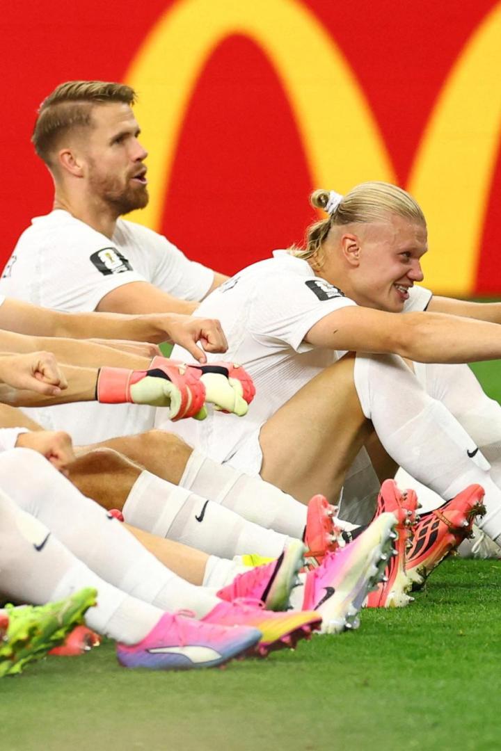 Die norwegische Nationalmannschaft jubelt sitzend auf dem Rasen. Stürmer Erling Haaland streckt seine beiden Arme aus. 