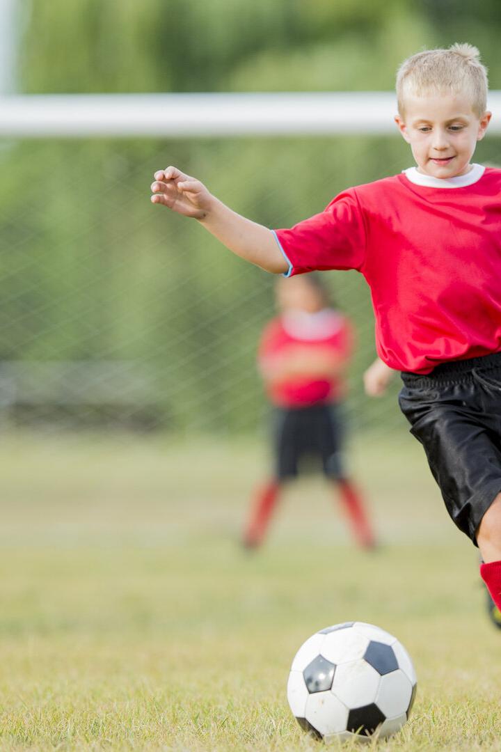Mehrere Kinder spielen Fußball, ein Junge in Rot läuft zum Ball.