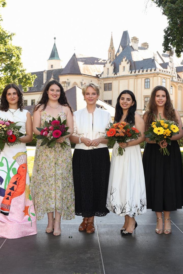 Sechs Personen mit Blumensträußen stehen vor einem Schloss neben einem Flügel im Freien.