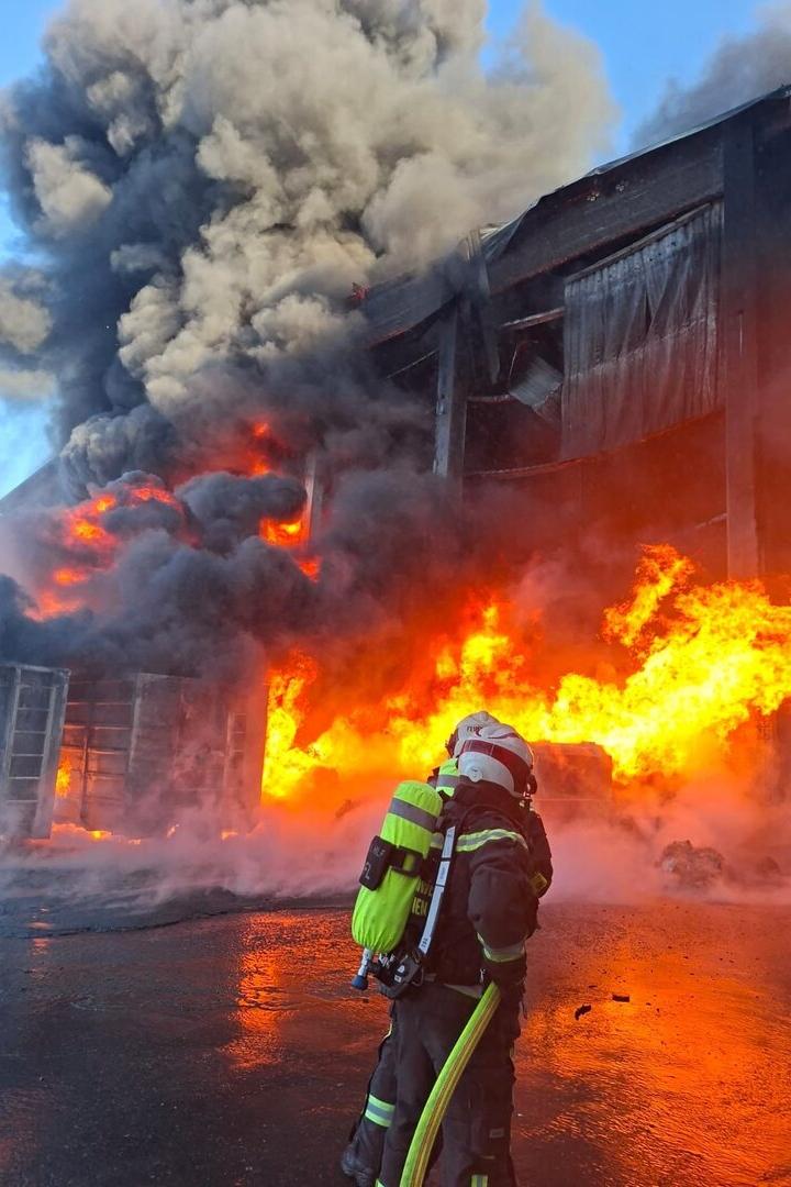Feuerwehrmann vor einem brennenden Gebäude mit dichtem Rauch und meterhohen Flammen.