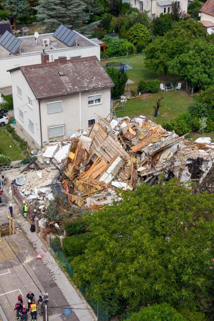 Ein eingestürztes Wohnhaus in einem Wohngebiet mit Einsatzkräften und einem Bagger vor Ort.