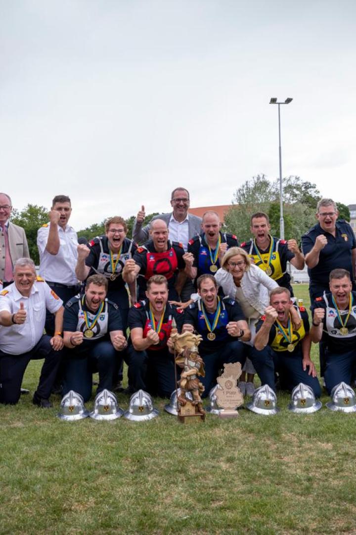Mehrere Personen stehen gemeinsam auf einer Wiese und freuen sich über den Sieg der Freiwilligen Feuerwehr in Trattenbach bei den Landesfeuerwehrbewerben