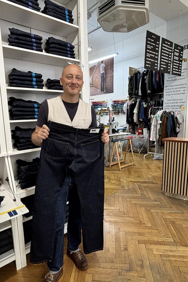Mann in Jeansladen hält eine sehr große dunkle Jeans vor sich.
