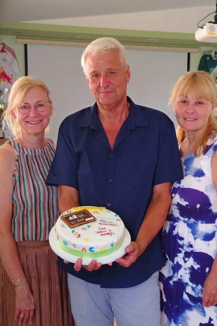 Drei Frauen und ein Mann stehen lächelnd zusammen, während der Mann eine Torte mit der Aufschrift „42“ hält.