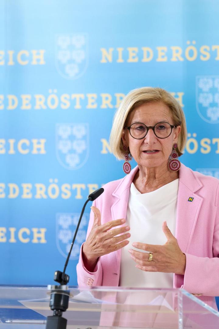 Johanna Mikl-Leitner steht vor einem Rednerpult und spricht in ein Mikrofon, hinter ihr ist eine blaue Wand, auf der mit gelben Buchstaben Niederösterreich steht
