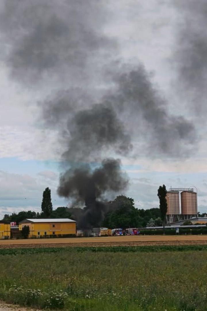 Dichter schwarzer Rauch steigt hinter Gebäuden auf, offenbar ein Brand auf einem Gelände im Grünen.