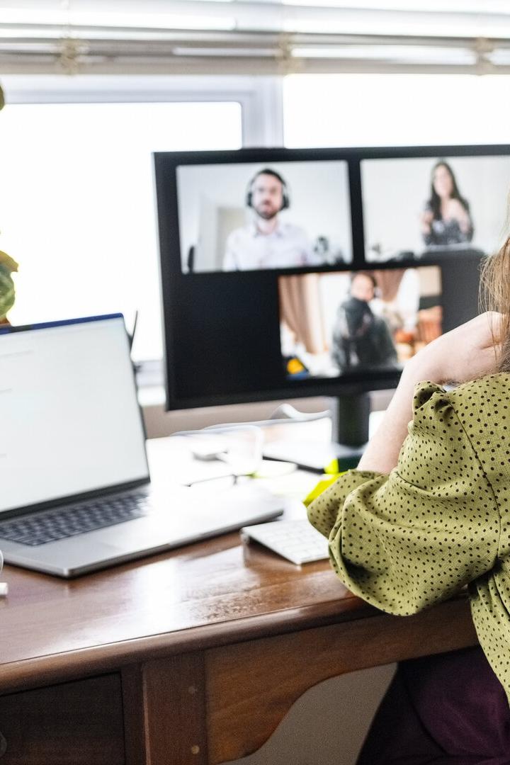 Frau im Homeoffice vor Laptop und Monitor bei Videokonferenz.