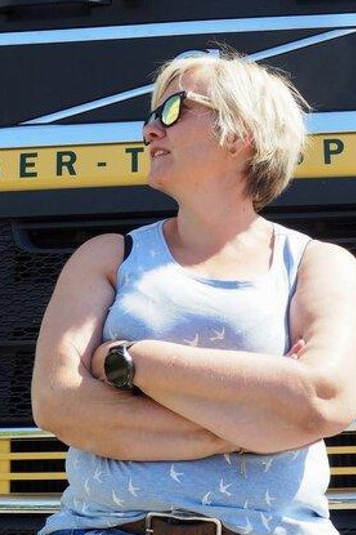 Eine Frau mit Sonnenbrille lehnt vor einem gelben Volvo-Lkw mit verschränkten Armen.