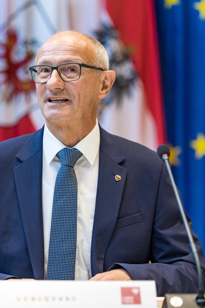 Anton Mattle spricht vor österreichischen und europäischen Flaggen an einem Pult mit der Aufschrift „Bergauf für Österreich“.