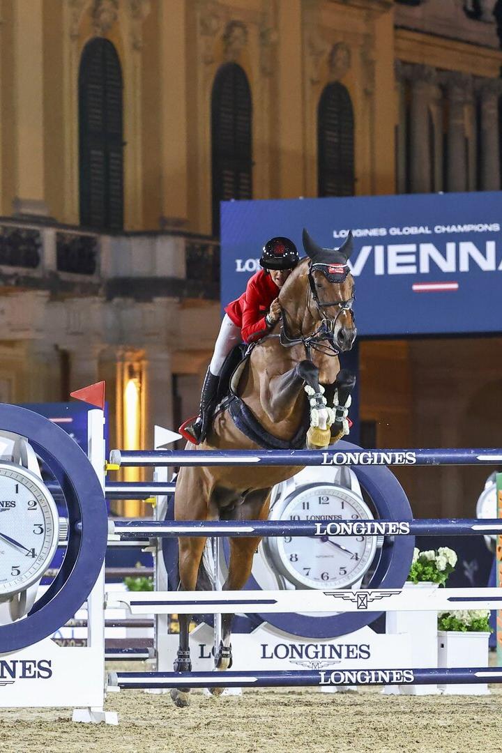 Springreiter überwindet ein Longines-Hindernis bei Nacht vor historischer Fassade.