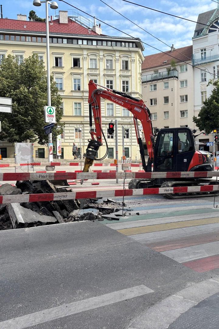 Bagger bei Straßenbau an einer gesperrten Kreuzung mit aufgerissener Fahrbahn.