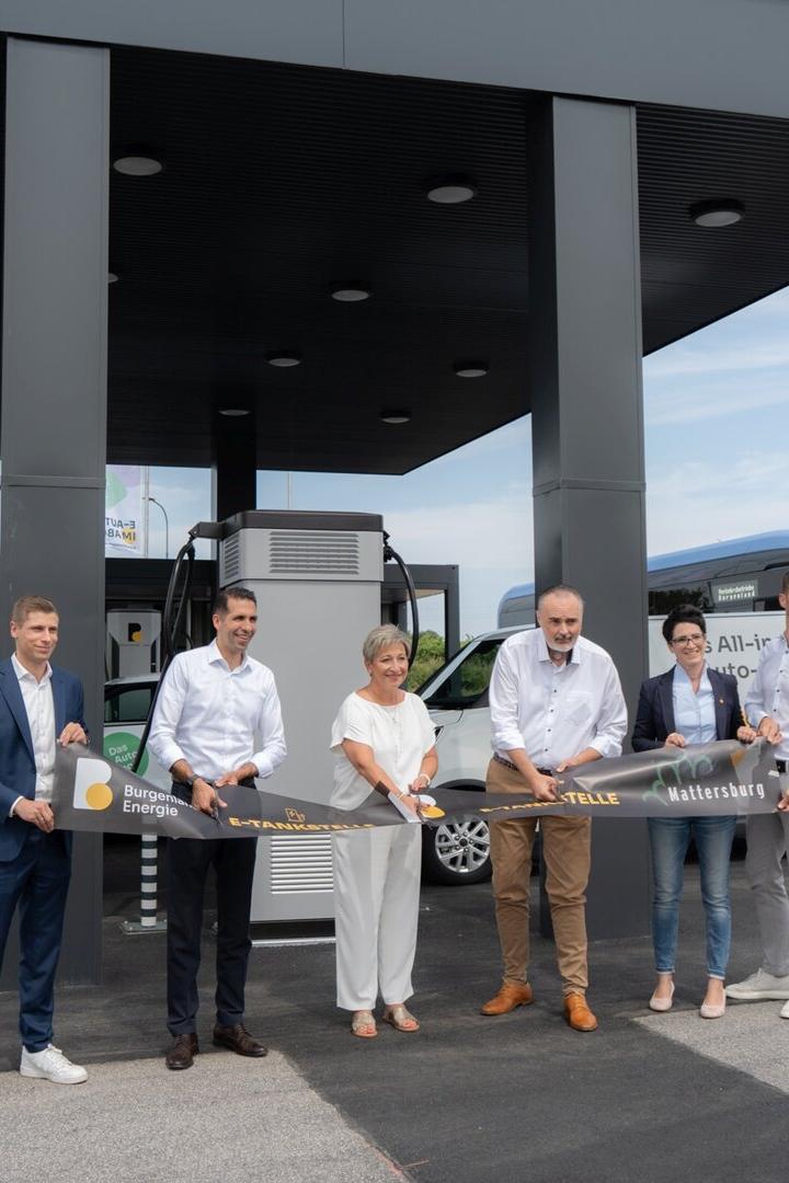 Sechs Personen durchschneiden feierlich ein Band zur Eröffnung einer E-Tankstelle der Burgenland Energie in Mattersburg.