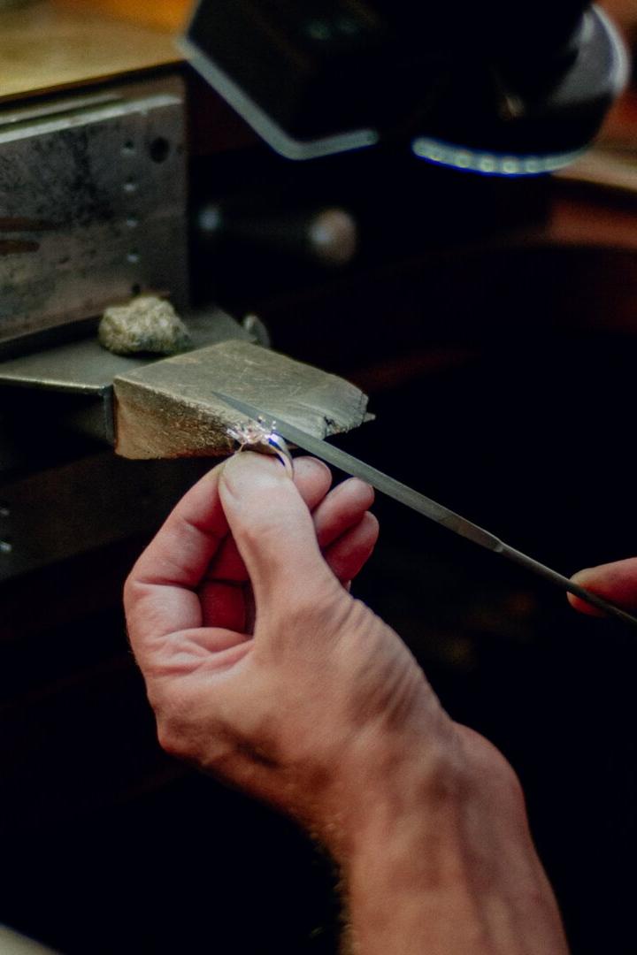 Ein Goldschmied bearbeitet mit einer Feile einen Ring auf einem Werktisch.