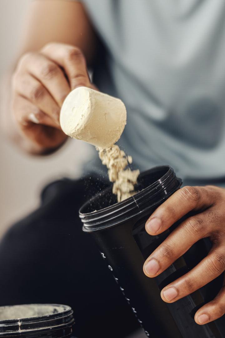 Person adding protein powder to shaker for fitness