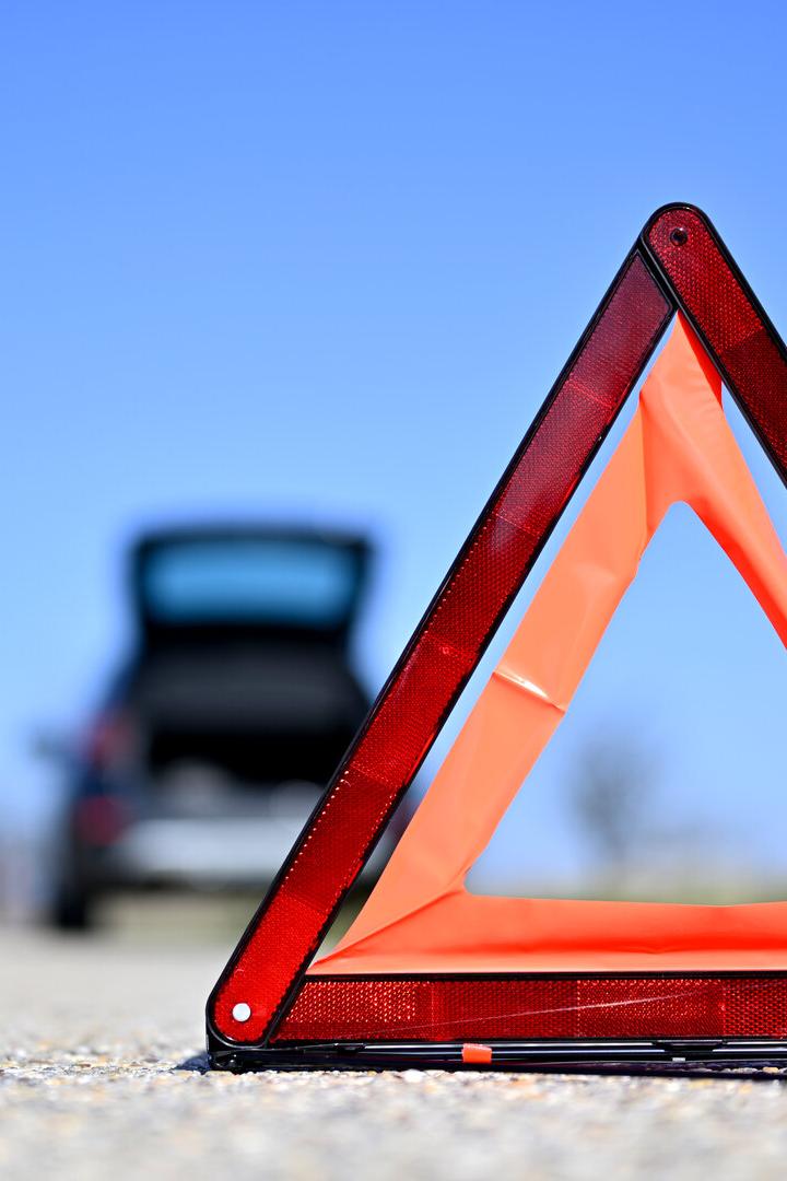 Ein rotes Warndreieck steht auf einer Straße vor einem Auto mit geöffnetem Kofferraum.