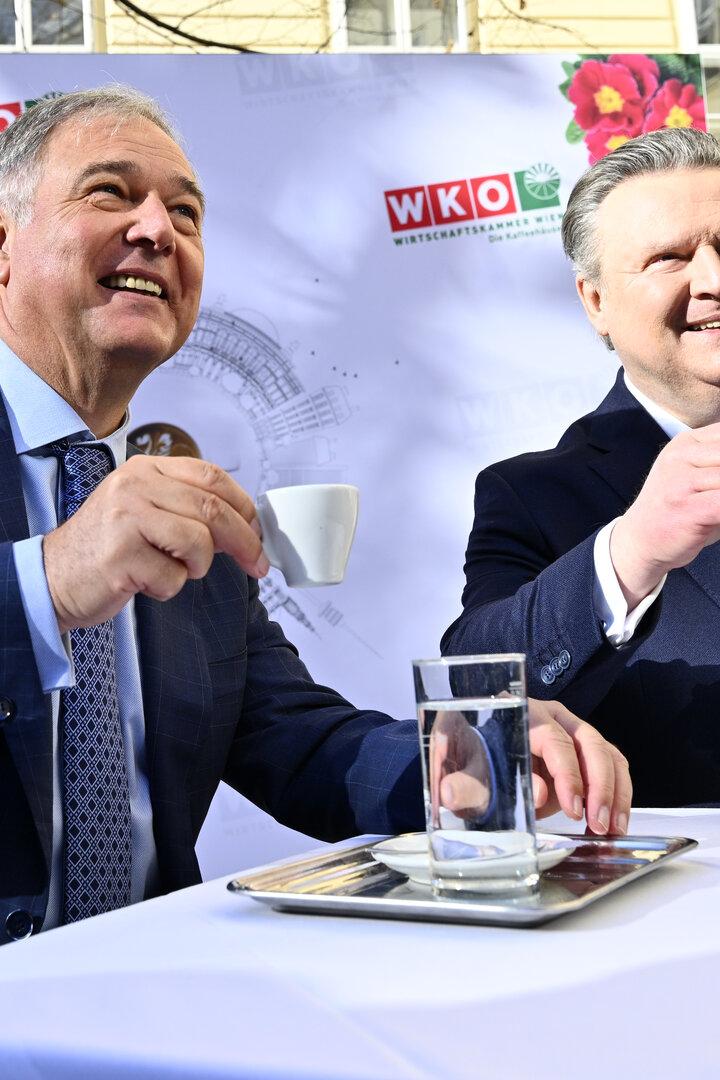 Walter Ruck und Michael Ludwig im Anzug trinken im Freien Espresso an einem Tisch vor einem WKO-Hintergrund.