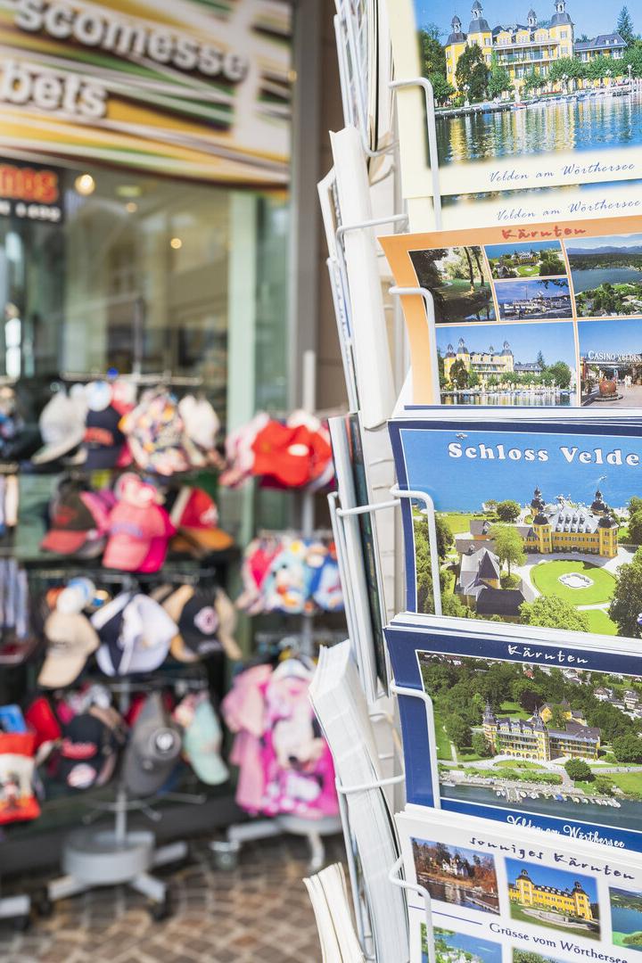 Postkartenständer vor einem Souvenirshop mit Ansichten vom Wörthersee und Schloss Velden.
