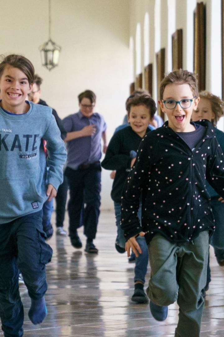 Kinder laufen fröhlich durch einen Klostergang.