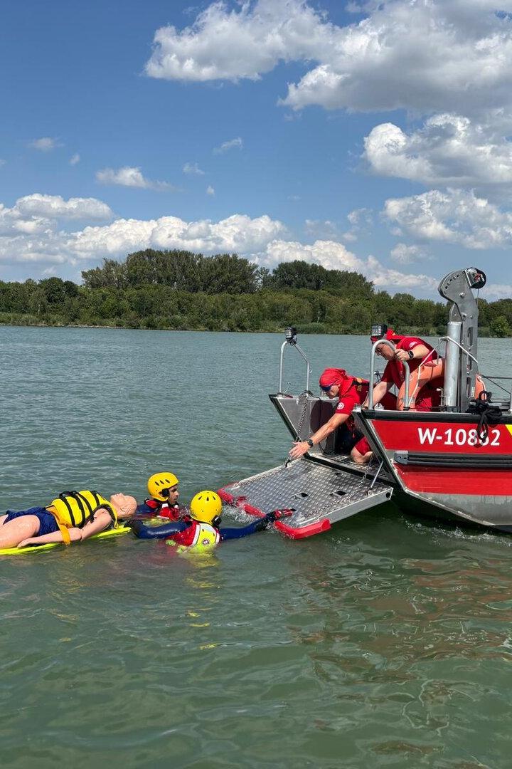 Zwei Rettungsschwimmer in gelben Helmen bergen eine Übungspuppe auf einer Trage vom Rettungsboot „Susanne“ der Samariter aus dem Wasser.