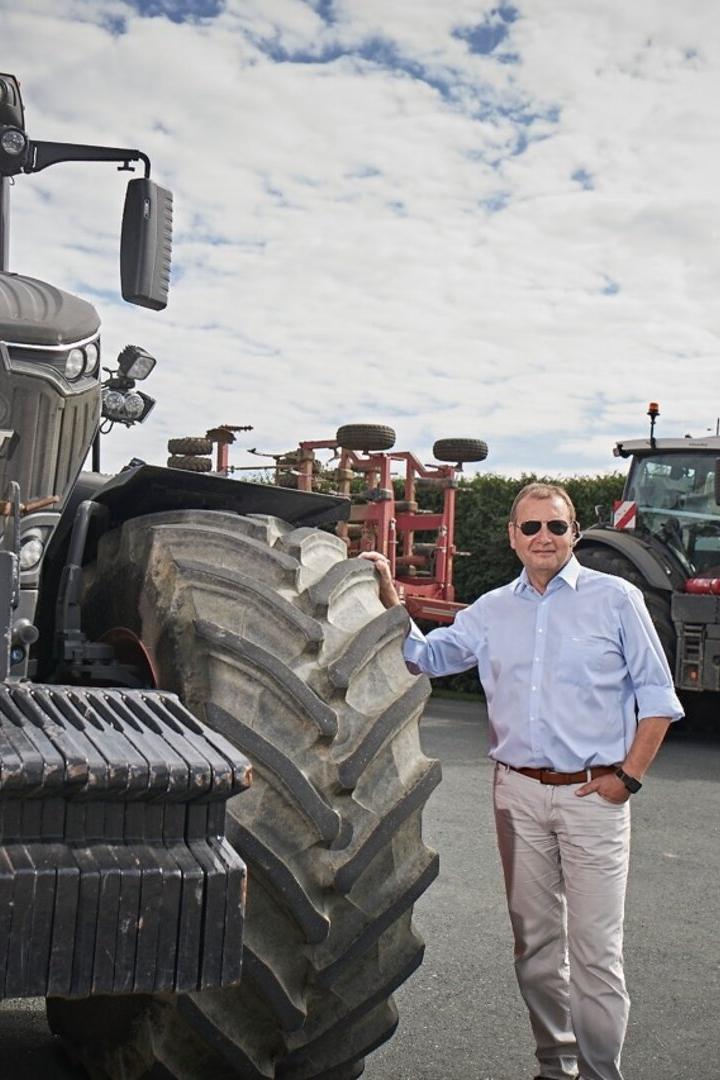 Mann in hellblauem Hemd steht neben großem Fendt-Traktor auf einem Hof.