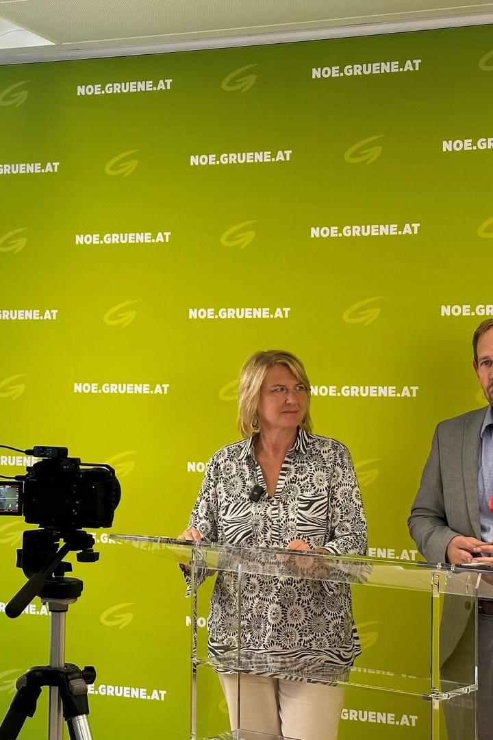 Zwei Politiker sprechen an einem Rednerpult vor grünem NOE.GRUENE.AT-Hintergrund, eine Kamera filmt sie.